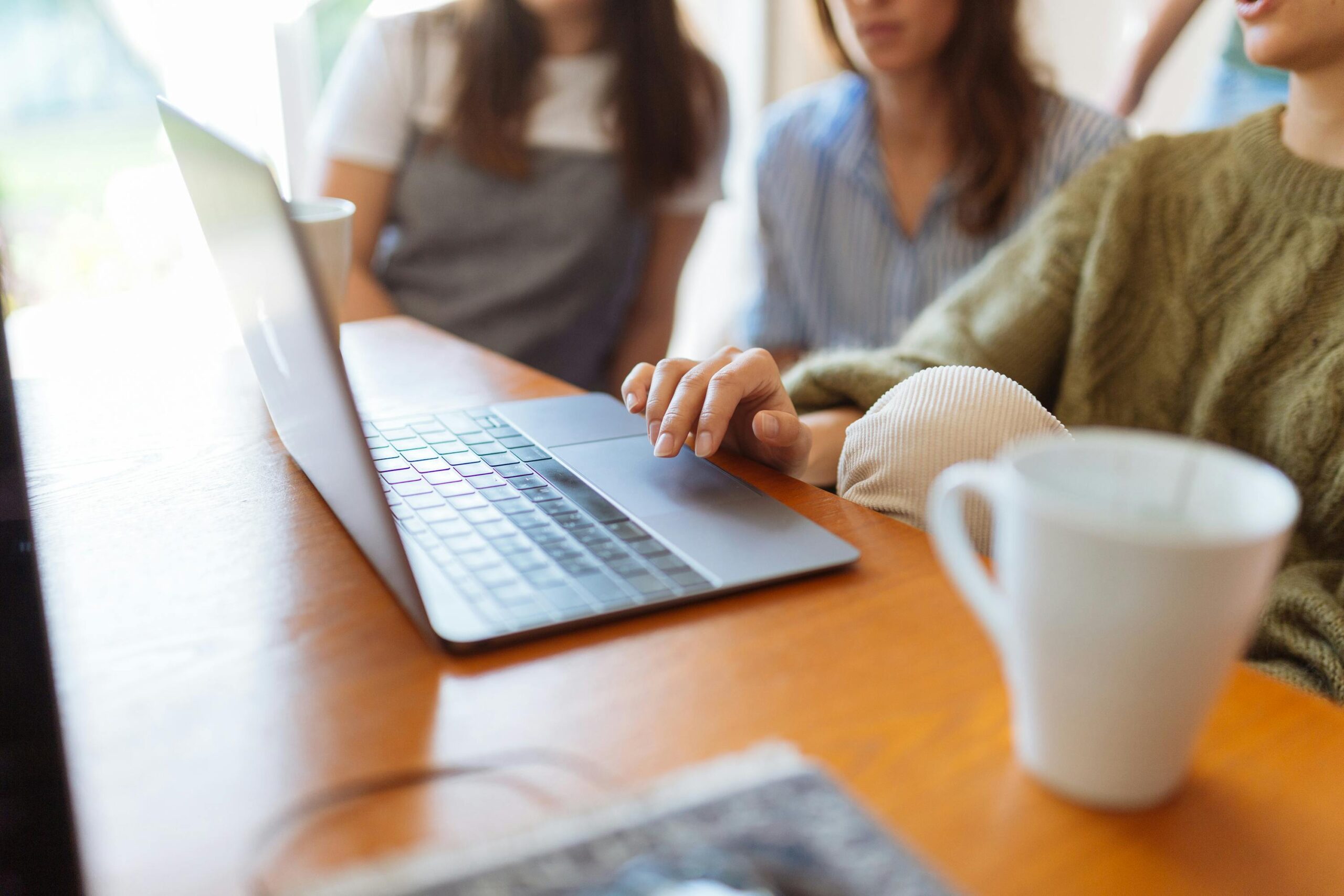 Group of women collaborating in a workspace with a laptop and coffee mugs on the table.